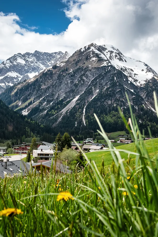 SuperLastMinute Juni 2025 Alpendorf mit schneebedeckten Bergen, Wiesen und traditionellen Holzhäusern